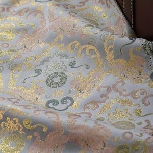 May include: Close-up of a light grey fabric with a repeating pattern of pink and gold swirls and circles. The fabric has a subtle shimmer.