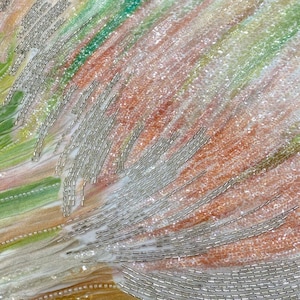 May include: A textile surface featuring a blend of soft green, peach, and white hues with a shimmering, glittery texture. The fabric is embellished with rows of thin, metallic silver bugle beads arranged in linear patterns across the surface.