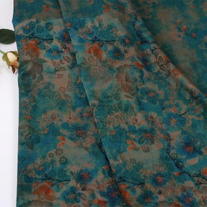 May include: A close-up of a fabric with a floral pattern. The fabric features a teal background with blue and orange floral designs. The fabric is folded, showing the texture and pattern variations.