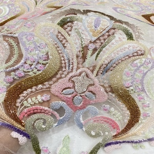 Könnte beinhalten: Nahaufnahme eines transparenten Stoffes mit aufwendigen Stickereien und Paillettenverzierungen. Das Design zeigt florale und Paisley-Motive in Rosa-, Blau-, Grün- und Goldtönen. Der Stoff hat ein zartes, strukturiertes Aussehen.