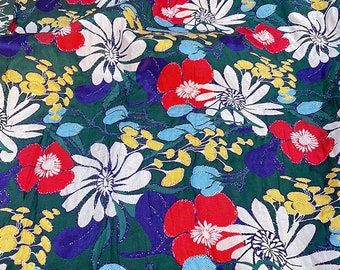 May include: A green fabric with a white, red, and yellow floral pattern. The fabric has a shiny, glittery texture.