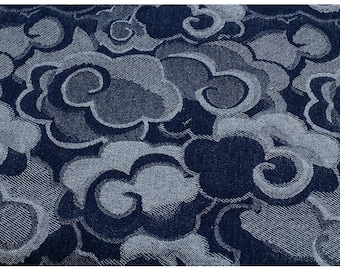 May include: Close-up of a fabric with a repeating cloud pattern. The design features swirling cloud shapes in shades of blue and gray, creating a textured, tonal effect. The fabric appears to be woven, with visible threads.