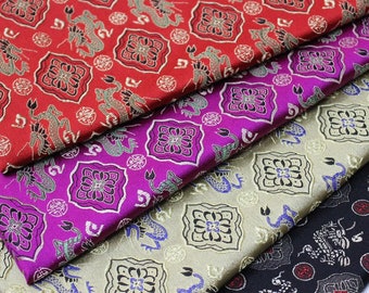 Op de afbeelding: Close-up van verschillende gevouwen stoffen met sierlijke patronen. De stoffen zijn in tinten rood, paars, goud en zwart. Elke stof heeft een herhalend ontwerp van draken en bloemmotieven, wat een luxueuze en gedetailleerde uitstraling creëert.