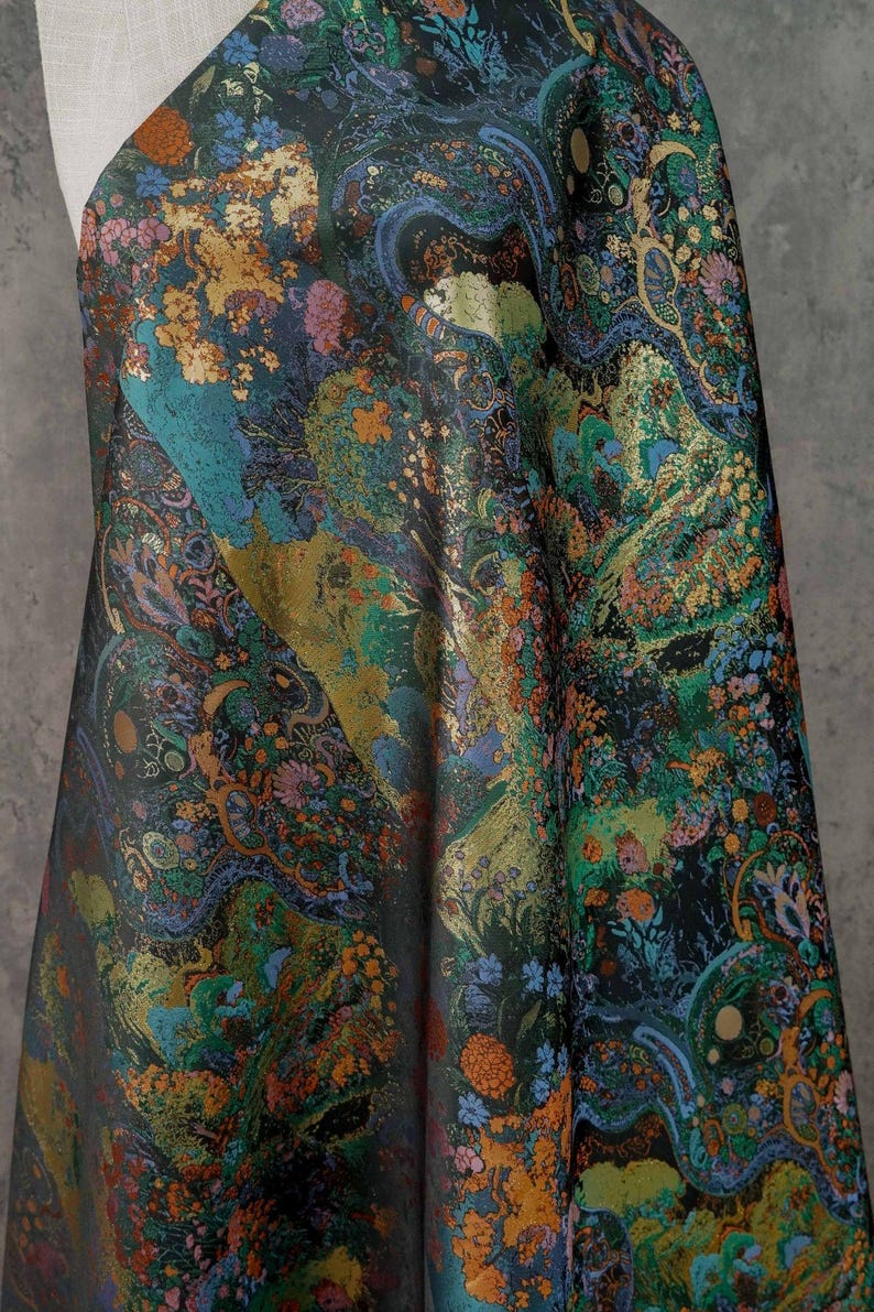 Puede incluir: Tela oscura con un intrincado estampado floral. El dise&ntilde;o presenta tonos dorados, turquesa, naranja y azul, creando una apariencia rica y texturizada. La tela drapeada muestra el estampado detallado.