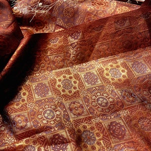 Pode incluir: Close-up de um tecido vermelho e dourado com um padrão geométrico repetitivo. O tecido tem um aspecto texturizado e tecido.