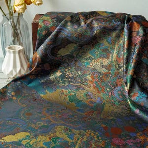 Puede incluir: Una tela drapeada con un dise&ntilde;o abstracto vibrante en tonos de verde azulado, dorado, naranja y morado. El textil tiene un brillo met&aacute;lico brillante, lo que sugiere un material lujoso. Ideal para ropa o decoraci&oacute;n del hogar.
