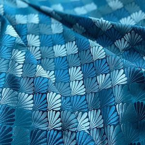 Peut inclure: Tissu turquoise avec un motif répété de coquillages stylisés blancs et bleus.