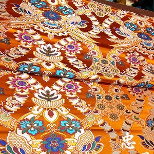 May include: Orange fabric with a white, gold, and multi-colored floral pattern. The fabric has a brocade texture.