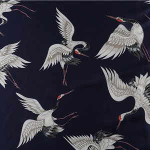Peut inclure: Tissu bleu marine fonc&eacute; avec un motif r&eacute;p&eacute;t&eacute; de grues blanches. Les grues ont des ailes grises, des accents noirs et des marques rouges sur la t&ecirc;te. Les oiseaux sont repr&eacute;sent&eacute;s en vol ou debout.