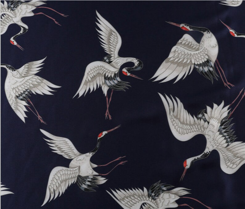Peut inclure: Tissu bleu marine fonc&eacute; avec un motif r&eacute;p&eacute;t&eacute; de grues blanches. Les grues ont des ailes grises, des accents noirs et des marques rouges sur la t&ecirc;te. Les oiseaux sont repr&eacute;sent&eacute;s en vol ou debout.