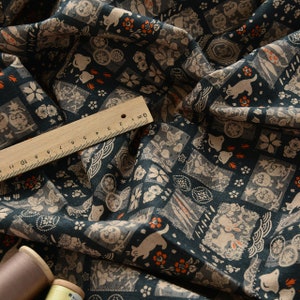 Op de afbeelding: Donkerblauwe stof met een herhalend patroon van witte en oranje Japanse geïnspireerde illustraties. Het patroon omvat dieren, bloemen en geometrische vormen. Een liniaal is inbegrepen voor de schaal.