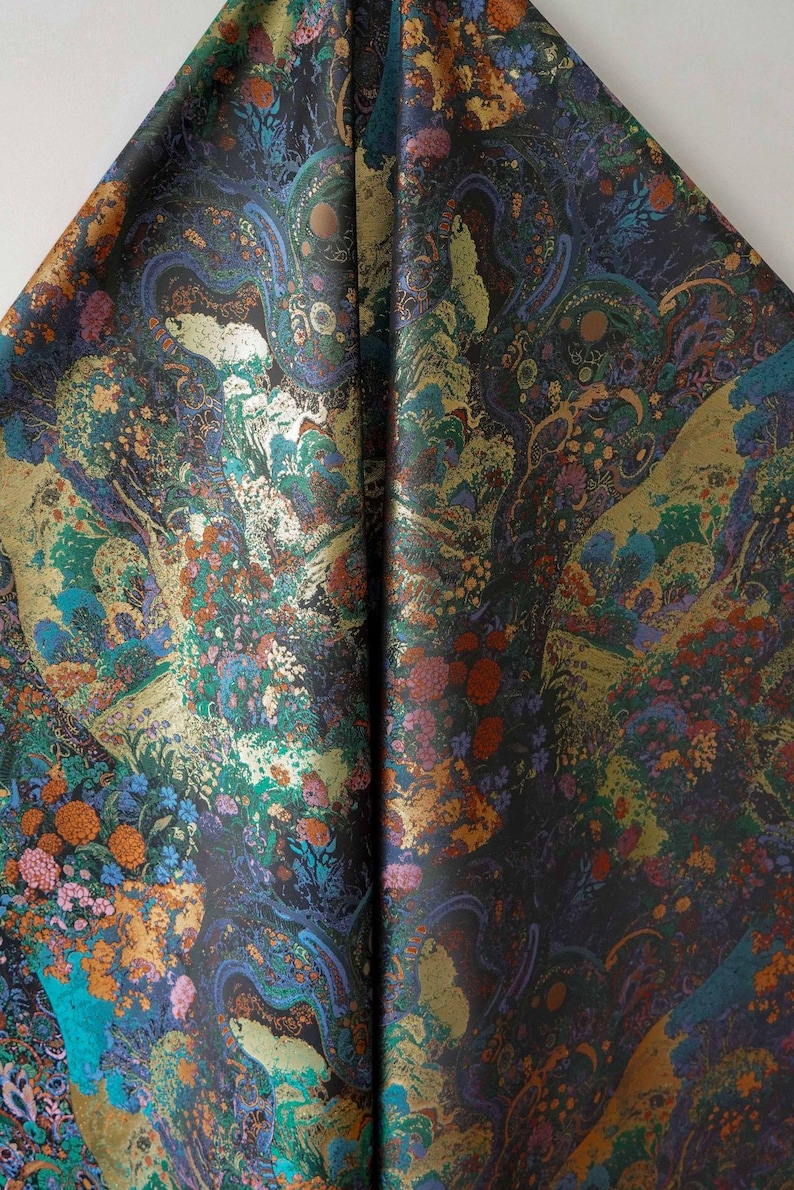 Puede incluir: Una tela doblada con un patr&oacute;n detallado y colorido. El dise&ntilde;o presenta una mezcla de elementos florales y abstractos en tonos de verde azulado, dorado, naranja y morado sobre un fondo oscuro. La tela tiene un brillo lujoso.