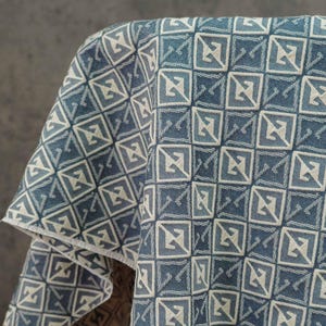Puede incluir: Tela estampada azul y blanca con un diseño geométrico. La tela está drapeada, mostrando el patrón cuadrado repetitivo con un motivo estilizado en forma de flecha. La paleta de colores incluye tonos de azul y blanco.