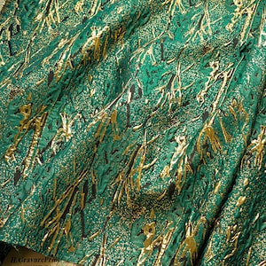 Könnte beinhalten: Grüner Stoff mit goldenem Metallic-Muster. Das Muster ähnelt Ästen oder Ranken.