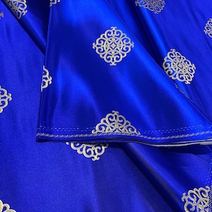 May include: Royal blue fabric with a repeating pattern of gold ornate designs. The fabric is folded and the gold designs are visible on both sides of the fold.