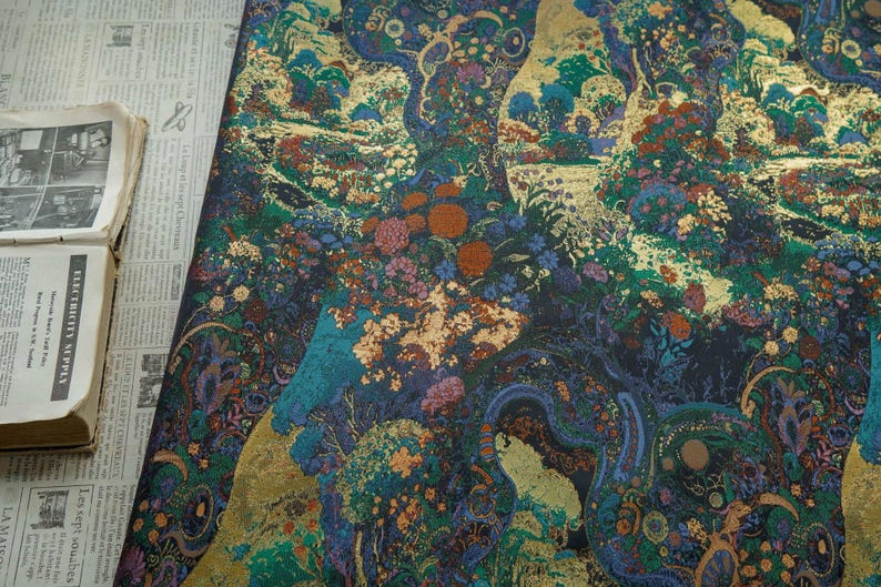 Puede incluir: Una tela detallada con un dise&ntilde;o floral colorido. El patr&oacute;n presenta una mezcla de azules, verdes, naranjas y dorado, creando un aspecto rico y texturizado. La tela es probablemente para tapicer&iacute;a o fines decorativos.
