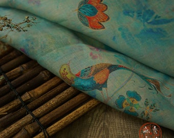 Könnte beinhalten: Ein hellblauer Stoff mit einem floralen und Vogelmuster. Der Stoff zeigt einen blauen und orangen Vogel mit langem Schwanz und eine blaue und orange Blume. Der Stoff liegt auf einer braunen Bambusmatte.