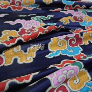 Könnte beinhalten: Marineblauer Stoff mit einem farbenfrohen Wolkenmuster in Gelb-, Rot-, Rosa-, Grün- und Blautönen. Der Stoff hat einen dezenten Glanz und ist aufwendig detailliert, mit einem fließenden, strukturierten Aussehen.