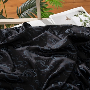 Könnte beinhalten: Schwarzer Satin-Stoff mit einem blauen Wolkenmuster. Der Stoff ist drapiert und gefaltet, wodurch die Textur und das Design sichtbar werden.