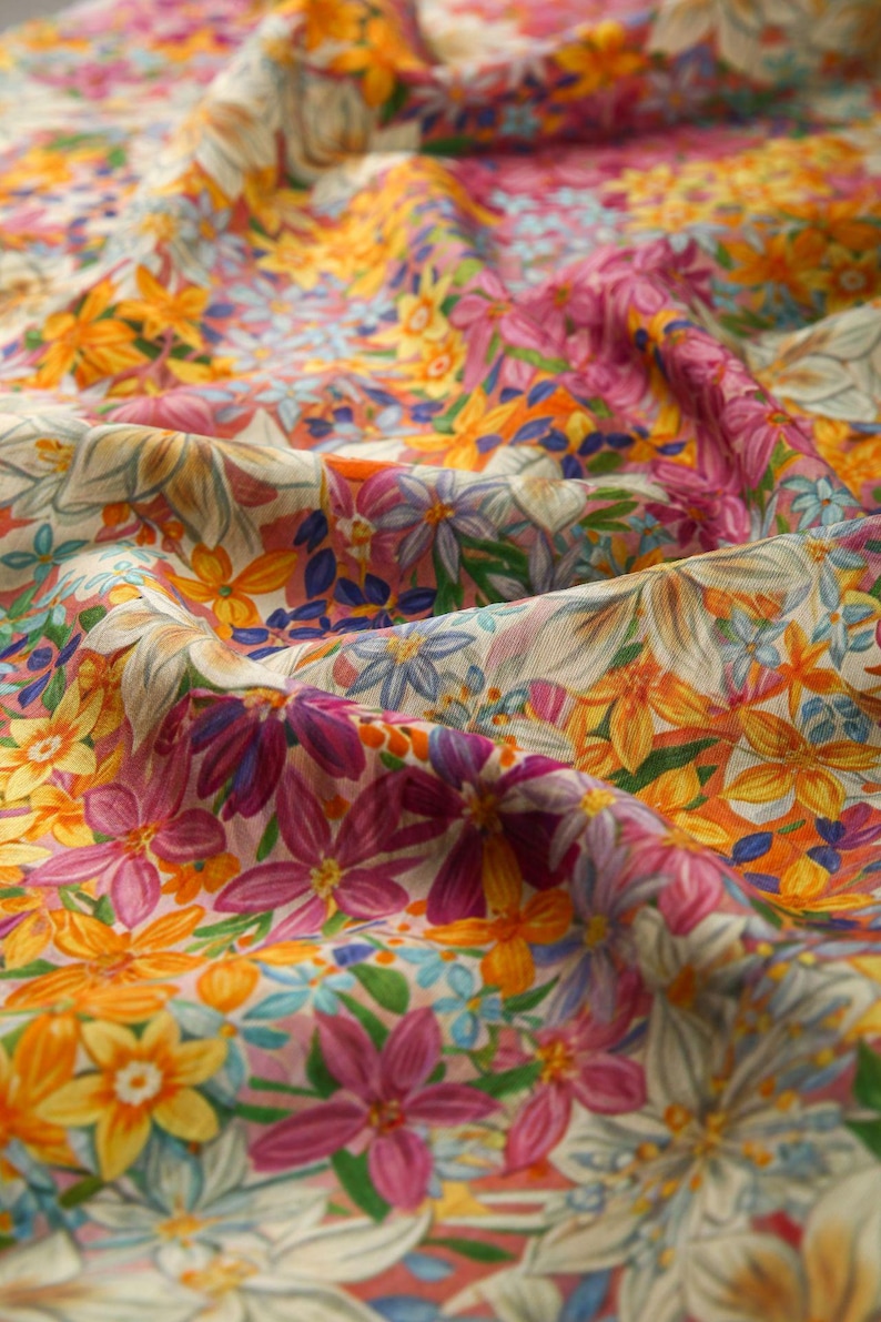 May include: A close-up of a fabric with a floral print. The fabric is a light beige color with a variety of flowers in shades of pink, yellow, orange, and blue.