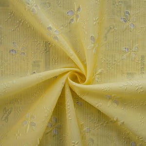 May include: Pale yellow sheer fabric with a delicate floral pattern. The fabric is soft and lightweight, making it ideal for curtains, tablecloths, or other decorative purposes.
