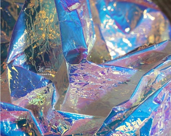 May include: Close-up of iridescent blue and purple fabric with a crinkled texture. The fabric is shiny and reflective, creating a holographic effect.
