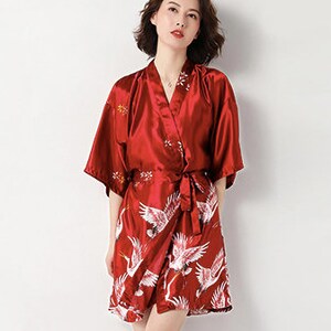 Peut inclure: Robe kimono en satin rouge avec un motif de grue. La robe pr&eacute;sente une conception enveloppante avec une ceinture assortie. Des grues blanches sont imprim&eacute;es sur la moiti&eacute; inf&eacute;rieure. Manches courtes et broderie florale pr&egrave;s de l'encolure.