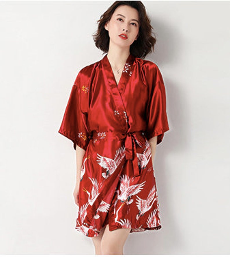 Peut inclure: Robe kimono en satin rouge avec un motif de grue. La robe pr&eacute;sente une conception enveloppante avec une ceinture assortie. Des grues blanches sont imprim&eacute;es sur la moiti&eacute; inf&eacute;rieure. Manches courtes et broderie florale pr&egrave;s de l'encolure.