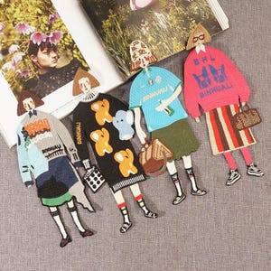 Pode incluir: Cinco patches bordados com figuras de desenhos animados de pessoas vestindo roupas diferentes. Os patches são todos de cores diferentes e têm o texto "Binhuai" neles.