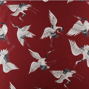 Peut inclure: Un tissu avec un motif r&eacute;p&eacute;t&eacute; de grues blanches, grises et noires sur un fond rouge fonc&eacute;. Les grues sont repr&eacute;sent&eacute;es dans diff&eacute;rentes poses, avec des ailes d&eacute;ploy&eacute;es et de longues pattes, cr&eacute;ant un design dynamique et &eacute;l&eacute;gant.