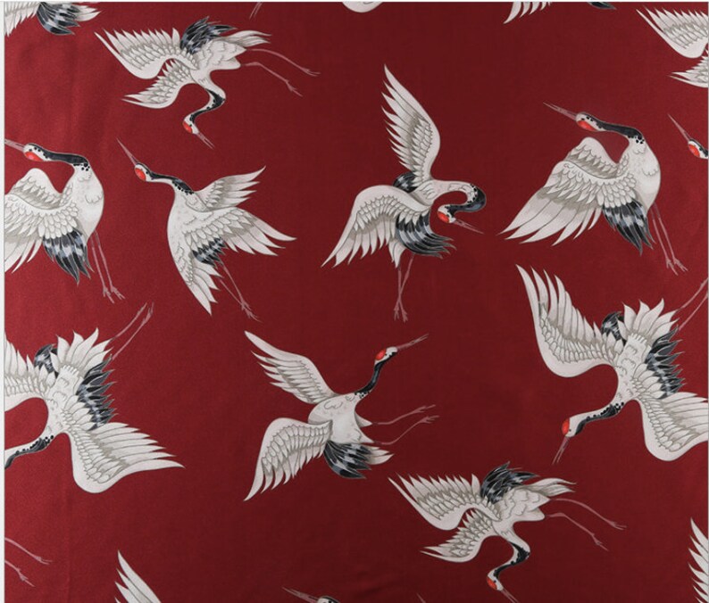 Peut inclure: Un tissu avec un motif r&eacute;p&eacute;t&eacute; de grues blanches, grises et noires sur un fond rouge fonc&eacute;. Les grues sont repr&eacute;sent&eacute;es dans diff&eacute;rentes poses, avec des ailes d&eacute;ploy&eacute;es et de longues pattes, cr&eacute;ant un design dynamique et &eacute;l&eacute;gant.
