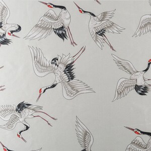 Peut inclure: Motif r&eacute;p&eacute;t&eacute; de grues stylis&eacute;es en vol. Les oiseaux sont repr&eacute;sent&eacute;s dans des tons de blanc, gris, noir et rouge, avec des ailes d&eacute;ploy&eacute;es et de longues pattes. Le fond est gris clair.