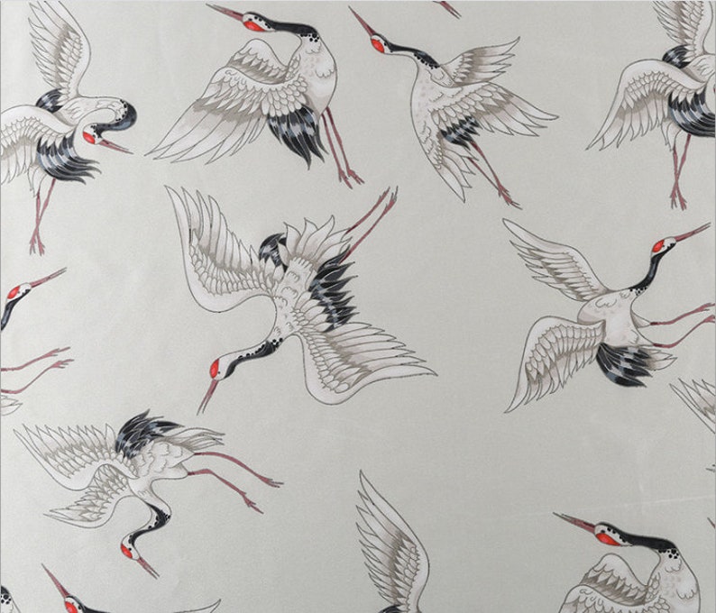Peut inclure: Motif r&eacute;p&eacute;t&eacute; de grues stylis&eacute;es en vol. Les oiseaux sont repr&eacute;sent&eacute;s dans des tons de blanc, gris, noir et rouge, avec des ailes d&eacute;ploy&eacute;es et de longues pattes. Le fond est gris clair.