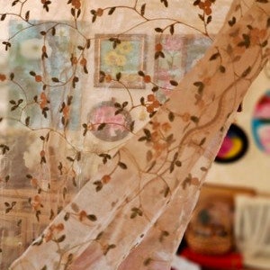 May include: A sheer curtain with a floral pattern in shades of brown and beige. The curtain is made of a delicate fabric and has a flowing, romantic look.