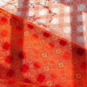 Puede incluir: Tela roja con un patrón geométrico dorado. La tela tiene un brillo sutil y una textura tejida.