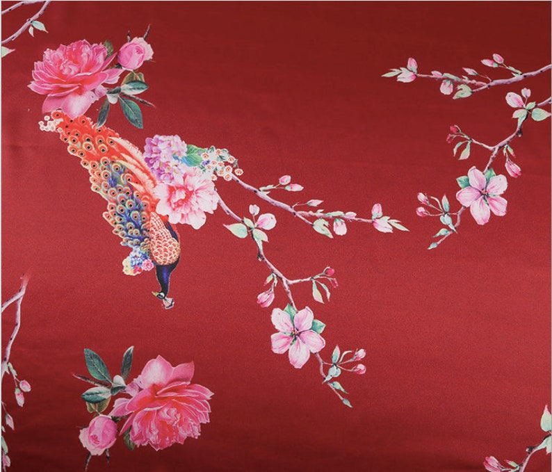 Peut inclure: Un tissu rouge avec un motif floral et paon. Le motif pr&eacute;sente un paon avec une queue color&eacute;e, des roses roses et des branches d&eacute;licates avec des fleurs roses et des feuilles vertes. Le fond est rouge fonc&eacute; uni.