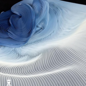 May include: Abstract textile art in shades of blue and white. The fabric is intricately pleated, creating a wave-like pattern. The design transitions from deep blue to light blue and white, with a logo in the bottom left corner.
