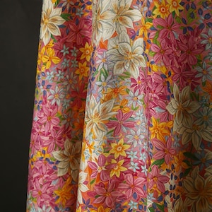 May include: A pink fabric with a floral pattern featuring white, yellow, and pink flowers. The fabric has a textured surface and a subtle sheen.