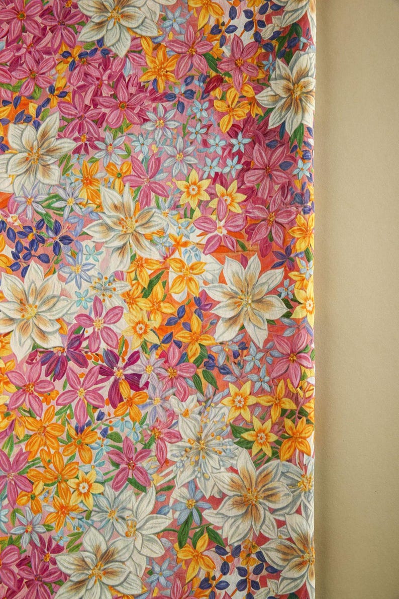 May include: A pink fabric with a floral pattern featuring white, yellow, and pink flowers. The fabric is covered in a variety of flowers, creating a busy and colorful design.