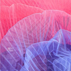 May include: Close-up of a pink and blue tulle fabric. The fabric is layered and has a gradient effect, transitioning from pink to blue.