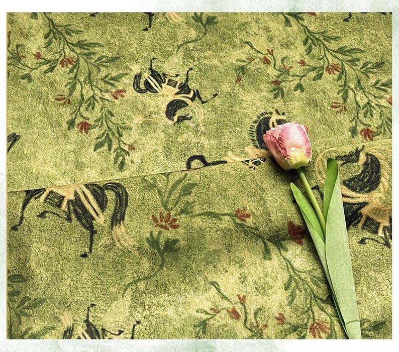 Może przedstawiać: Zbliżenie zielonej tkaniny z powtarzającym się wzorem czarnych koni i element&oacute;w kwiatowych. Tkanina ma teksturowany wygląd. R&oacute;żowy i ż&oacute;łty tulipan z zielonymi liśćmi znajduje się na pierwszym planie.