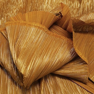 Può includere: Tessuto plissettato dorato con un effetto metallico. Il tessuto è piegato e drappeggiato, mostrando la trama e la lucentezza del materiale.