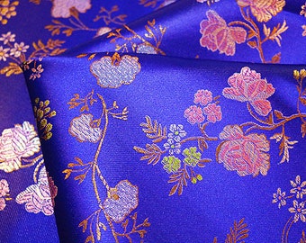 May include: Blue fabric with a floral pattern in gold, pink, and white. The fabric has a satin-like sheen.