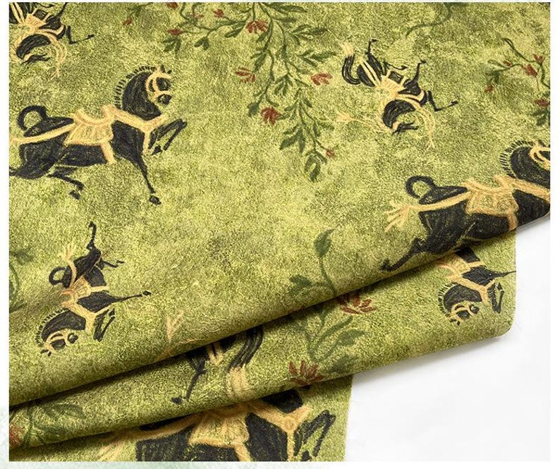 Może przedstawiać: Zielona tkanina z powtarzającym się wzorem czarnych koni z beżowymi siodłami i kwiatowymi akcentami. Tkanina ma teksturowany wygląd, z końmi w r&oacute;żnych pozach. Og&oacute;lny projekt ma estetykę vintage lub antyczną.