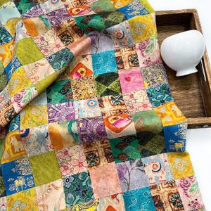 Pode incluir: Um tecido patchwork colorido com uma variedade de padrões e cores, incluindo desenhos florais, geométricos e de animais. O tecido é drapeado sobre uma bandeja de madeira, com uma tigela de cerâmica branca na bandeja.