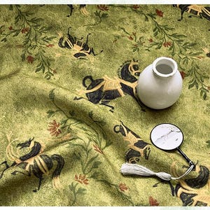 Może przedstawiać: Jasnozielona tkanina z powtarzającym się wzorem czarnych koni i element&oacute;w kwiatowych. Na tkaninie znajduje się mały biały wazon i lupa z chwostem.