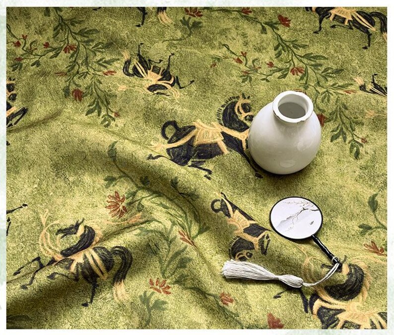 Może przedstawiać: Jasnozielona tkanina z powtarzającym się wzorem czarnych koni i element&oacute;w kwiatowych. Na tkaninie znajduje się mały biały wazon i lupa z chwostem.