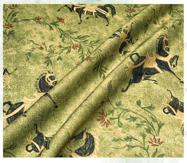 Może przedstawiać: Zielona tkanina z powtarzającym się wzorem czarnych koni ze złotymi akcentami, kwiatowymi pnączami i małymi czerwonymi kwiatami. Tkanina ma teksturowany wygląd i jest złożona, pokazując powtarzalność wzoru.
