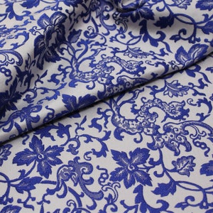 May include: White fabric with a blue floral pattern. The fabric has a textured, woven look.