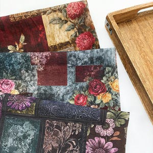 Puede incluir: Una variedad de piezas de tela con estampados florales en tonos burdeos, verde azulado y marrón, con rosas y otras flores. Una bandeja de madera con detalles metálicos se encuentra en el fondo.